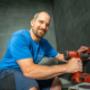 Handwerkliche Installation im Sanitärbereich: Eine Fachkraft arbeitet mit einer Bohrmaschine an einer gefliesten Badezimmerwand und richtet Bauteile präzise mit einer Wasserwaage aus. Die Arbeitskleidung mit Hauenstein‑Branding deutet auf professionel