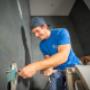 Montagearbeiten im Sanitärbereich: Eine Fachkraft installiert Leitungen und Anschlüsse in einem modern gefliesten Bad. Im Vordergrund sind Installationsmaterialien und ein Sanitärbauteil sichtbar, während die Arbeitskleidung mit Hauenstein‑Branding