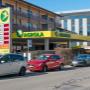AGROLA Tankstelle in Zug; auf linker Seite Tankstelle hinter geparkten Autos; grosses Totem mit AGROLA Logo und digitalen Preisschildern sowie Selfwash Logo
