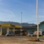 AGROLA Tankstelle in Reinach; links Tankstelle mit TopShop; grosse Überdachung; blaues Gebäude angeschlossen; rechts Mast im Vordergrund daneben Totem mit Landi Schild, AGROLA Schild und Preisanzeigen