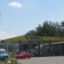 AGROLA Tankstelle in Buchrain mit TopShop; links grosses Totem-Schild mit Landi Logo, AGROLA Diskus Logo, digitaler Preisanzeige, AdBlue, TopShop und selfwash logo, vor Tankstelle rotes Auto