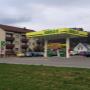 AGROLA Tankstelle in Bütschwil - freistehend mit zwei Tanksäulen. Links Totem mit AGROLA Logo und digitaler Preisanzeige. Dahinter Wohnüberbauung und Parkplatz
