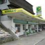 AGROLA Tankstelle in Rüegsbach, bei Autogarage; leicht gebogenes Dach mit Logo-Schild angebracht, zwei Tanksäulen, rechts Autogarage, links Treppe zu Wohnhaus