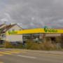 AGROLA Tankstelle in Rickenbach Sulz; diesige Aufnahme; vorne Strasse mit Fussgängerstreifen; links Totem mit AGROLA Logo und digitaler Preisanzeige; dahinter Wohnhäuser; rechts Tankstellendach