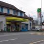 AGROLA Tankstelle in Trübbach. Im Vordergrund Strasse mit Fussgängerstreifen. TAnkstelle mit zwei Tanksäulen an Gebäudefassade. Grosses Totem mit AGROLA Logo und digitaler Preisanzeige.