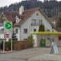 AGROLA Tankstelle in Zuckenriet (Niederhelfenschwil). Vor Wohnhaus Tankstelle mit kleiner Überdachung. Eine Tanksäule. Im Vordergrund Auffahrtstrasse mit Schild.