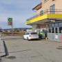 AGROLA Tankstelle in Kradolf-Schönenberg; vor Tankstelle weisses Auto; über Tankstellen-Dach Balkon; links Totem mit AGROLA Schild und digitaler Preisanzeige; dahinter Landwirtschafts-Feld