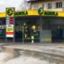 AGROLA Tankstelle in Liebefeld mit TopShop; regnerische Aufnahme; Tankstelle bei Kreisel gelegen; links Totem mit AGROLA Logo, digitaler Preisanzeige, AdBlue und TopShop Logo darunter