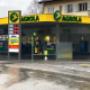 AGROLA Tankstelle in Liebefeld mit TopShop; regnerische Aufnahme; Tankstelle bei Kreisel gelegen; links Totem mit AGROLA Logo, digitaler Preisanzeige, AdBlue und TopShop Logo darunter