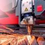 Eine hochpräzise Laserschneidmaschine schneidet ein Metallblech. Der Laser erzeugt dabei sichtbare Funken, was auf hohe Energie und Präzision hinweist.