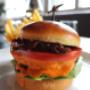 Timeout-Burger - Saftiges Rindfleisch, geschmolzener Cheddar, karamellisierte Zwiebeln, knackiger Lattich, frische Tomaten und unsere hausgemachte Burgersauce im fluffigen Brioche-Bun. Dazu knusprige Pommes.